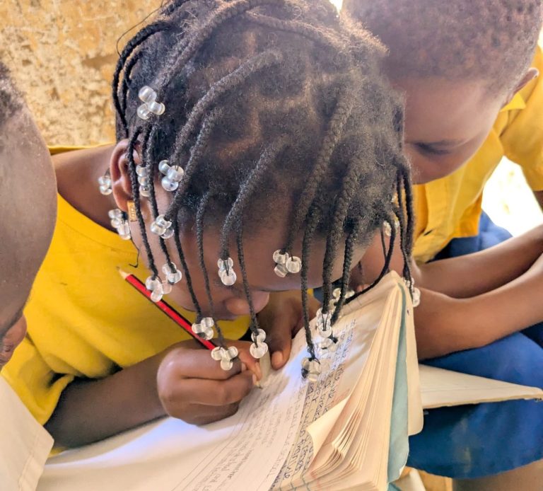 Children in yellow shirts focused on writing in a book.