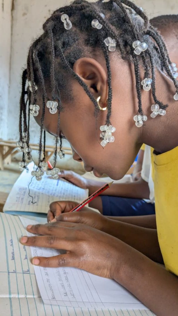 A girl in a yellow shirt writes in a notebook with concentration. 